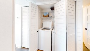 A compact laundry room with a washing machine and a shelf with folded towels and baskets.