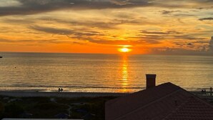 A sunset over the ocean with a beach in the foreground and a building with a sloped roof.