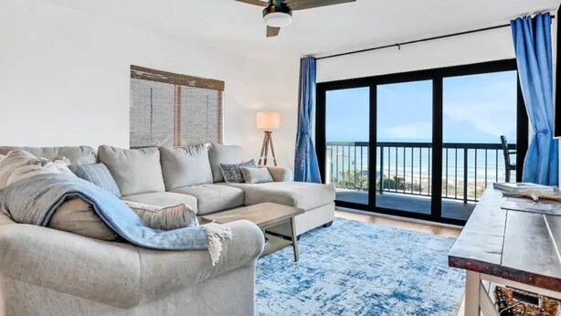 A living room with a sofa, a coffee table, a lamp, and a view of the outdoors through large windows.
