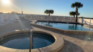 A swimming pool with a hot tub, palm trees, and a clear sky.