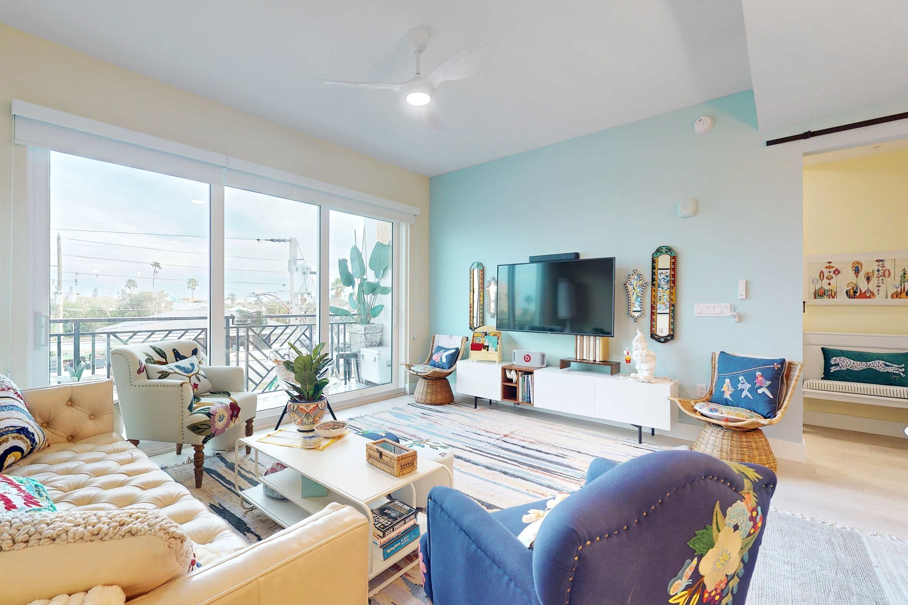 A spacious living room with a large window, a flat-screen TV, and a variety of seating options.