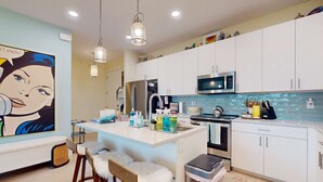 Een moderne keuken met witte kasten, een centraal kookeiland met barstoelen, een magnetron en een spoelbak.