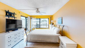 Une chambre avec un lit, une télévision, un ventilateur de plafond, une fenêtre et une vue sur le balcon.