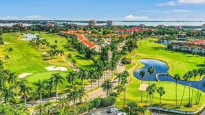 Un parcours de golf avec un obstacle d’eau, des palmiers et une vue sur un pont au loin.
