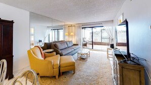 Un salon avec un canapé, un pouf et un téléviseur posé sur un meuble.