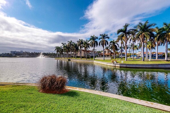 Un lago tranquilo con una fuente, rodeado de palmeras y edificios.