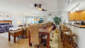 Un vaste espace de vie comprenant un coin repas avec une table en bois, des chaises en osier et une cuisine dotée de meubles en bois et d’un bar.