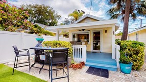 A small, single-story house with a porch, a dining table with chairs, and a small garden area. - Charming single level cottage with a kitchen enclosed yard and WiFi (Treasure Island)