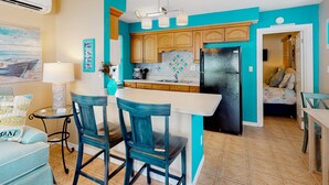 A kitchen with teal walls, wooden cabinets, a black refrigerator, and a bar area with two chairs. - Charming single level cottage with a kitchen enclosed yard and WiFi (Treasure Island)