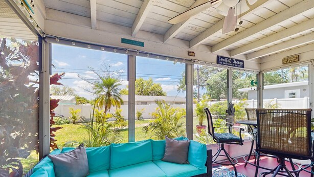 A covered outdoor seating area with a turquoise sofa, wicker chairs, and a patterned rug. - Inviting ranch home near the beach Florida room alfresco dining (Clearwater)