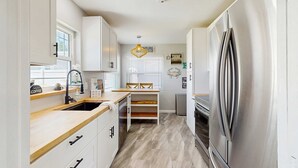 A modern kitchen with white cabinets, a stainless steel refrigerator, a wooden countertop, and a built-in bench. - Inviting ranch home near the beach Florida room alfresco dining (Clearwater)