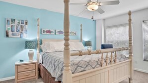 A bedroom with a four-poster bed, a nightstand with a lamp, and artwork on the walls.