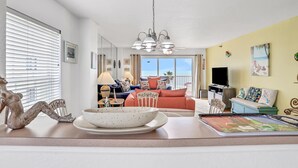 A living room with a sofa, a dining table with a bowl, and a chandelier.
