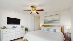 Ein Schlafzimmer mit einem Bett, einem Deckenventilator, einem Fernseher, einer Kommode und einem Bild an der Wand.
