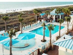 A pool area with lounge chairs and umbrellas, a beach view, and a building with a blue roof. - Marriott's SurfWatch Resort (Hilton Head Island)