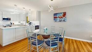 Une cuisine moderne avec des meubles blancs, un îlot central et un coin repas comprenant une table en verre et des chaises en métal.