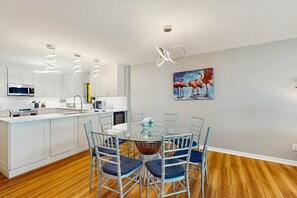 A modern kitchen with white cabinets, a central island, and a dining area with a glass table and metal chairs.