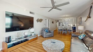 Un salon moderne avec un téléviseur à écran plat, un canapé gris, une table basse ronde et un ventilateur de plafond.