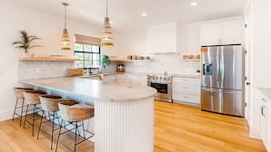 Cozinha moderna com ilha central, banquetas, eletrodomésticos de aço inoxidável e armários brancos.