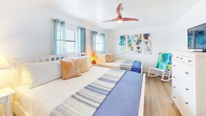 Une chambre avec deux lits, un ventilateur de plafond, une télévision et une commode.