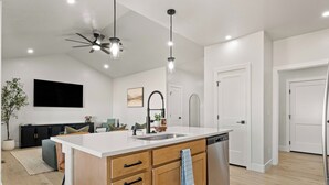 Una cocina moderna con una isla central, armarios de madera, lavavajillas empotrado e iluminación colgante.