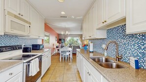 Una cocina moderna con armarios blancos, una isla central con pileta y salpicadero de azulejos.