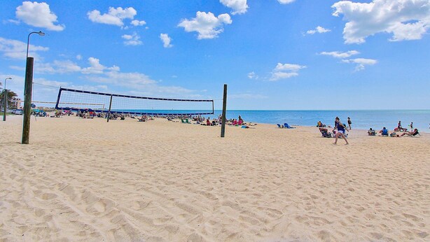 Un terrain de beach-volley avec un filet, entouré de sable et de personnes.