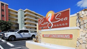 Naamplaatje voor Ram Sea Resort Condominiums, met een helder zicht op het uiterlijk van het gebouw en een geparkeerde witte SUV.
