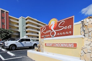 A sign for Ram Sea Resort Condominiums with a clear view of the building's exterior and a parked white SUV. - Oceanfront condo with heated pool hot tub and grills (North Redington Beach)