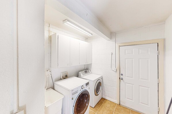 A laundry room with two washing machines, a dryer, a white door, and a light fixture.