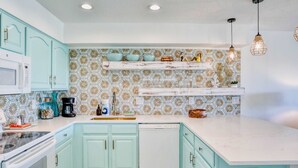 Cozinha com armários verde-água, lava-louças branco e painel de azulejos estampado.