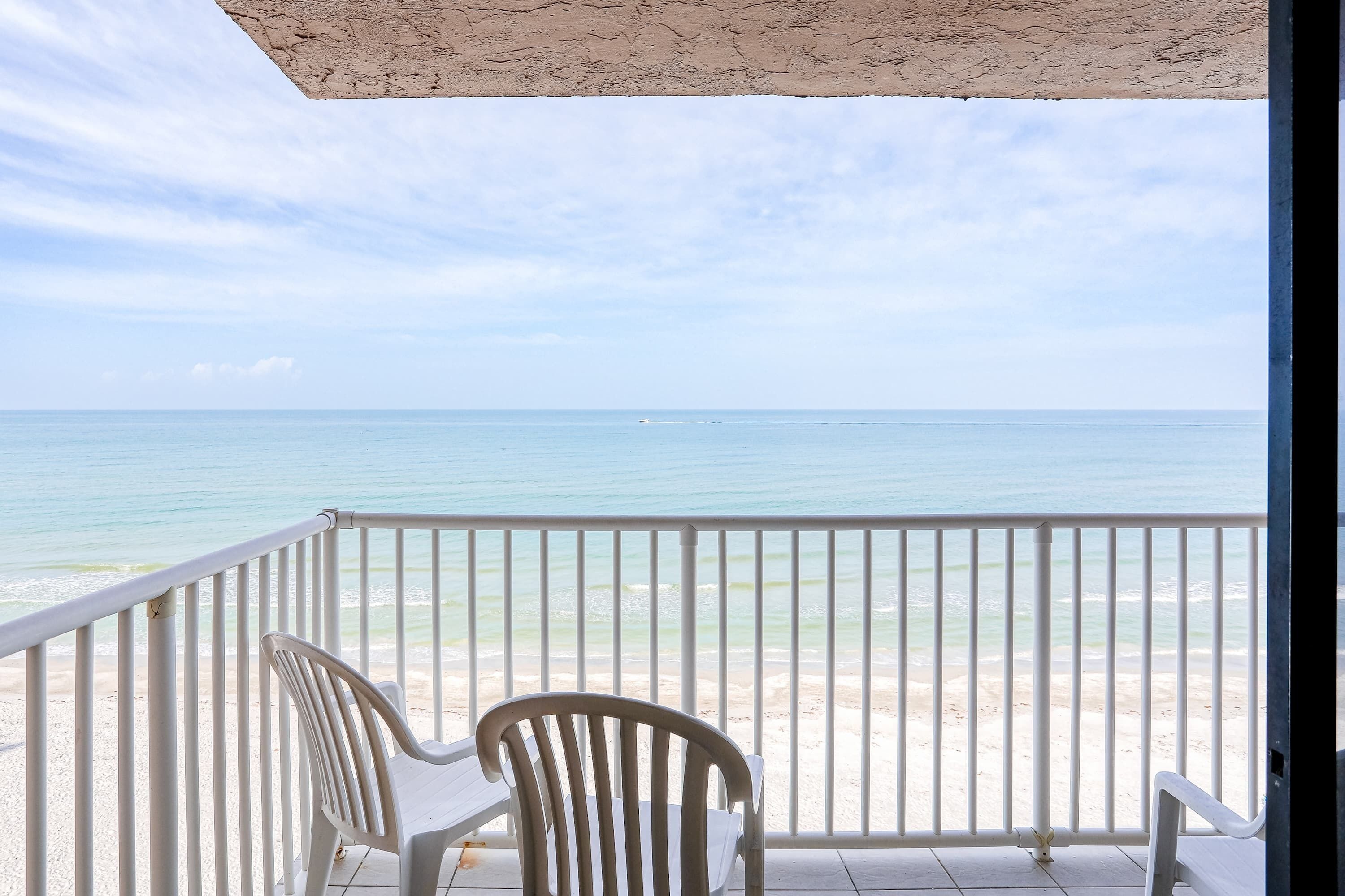 A balcony with white chairs overlooking a beach.