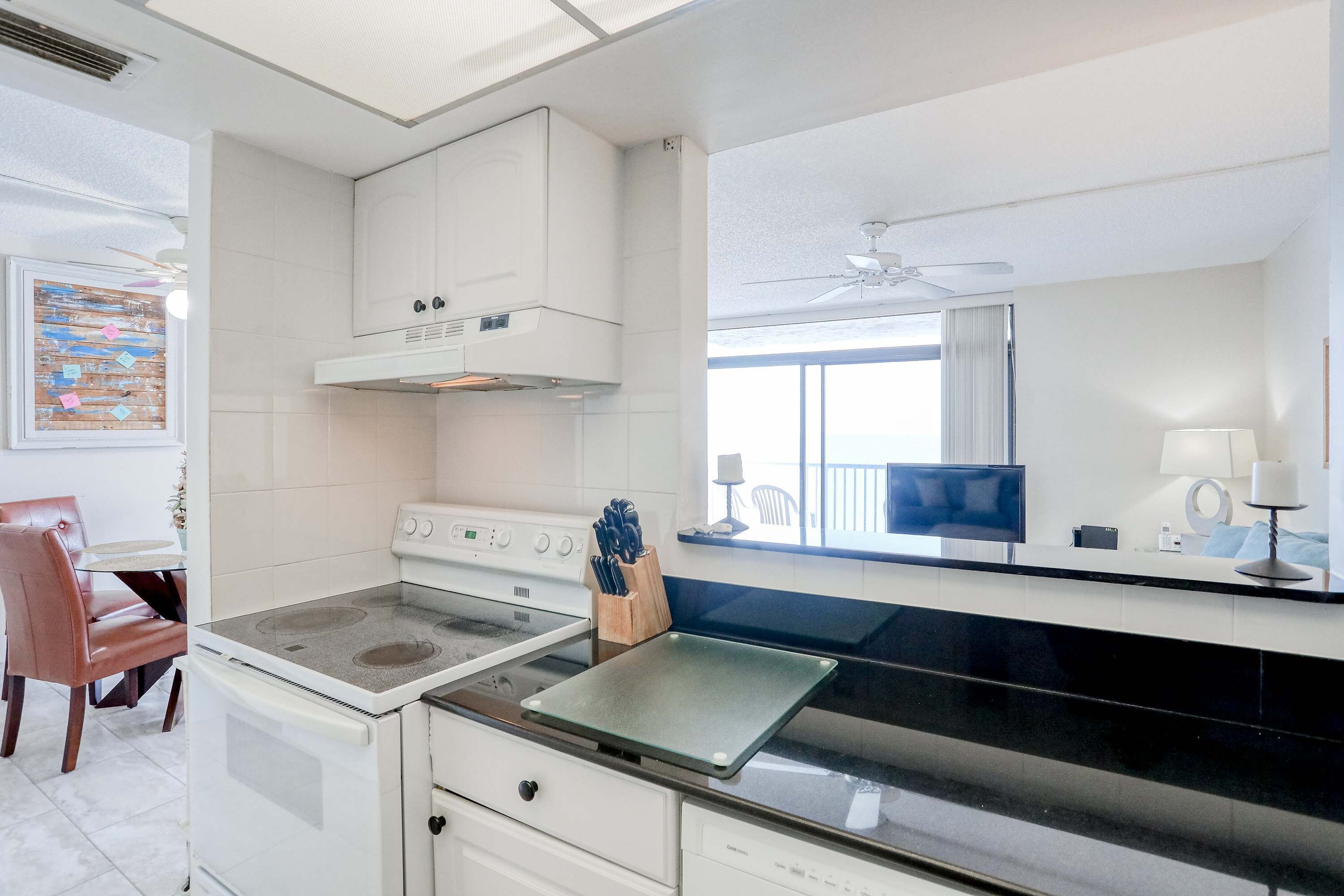 Une cuisine moderne équipée d’une cuisinière, d’un four et d’un four à micro-ondes. On y trouve un coin repas avec une chaise et une table. Un ventilateur de plafond est visible au-dessus du comptoir.