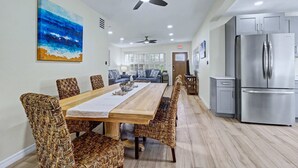 A modern kitchen with stainless steel appliances, a dining area with a wooden table and woven chairs, and a ceiling fan.