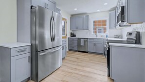 A modern kitchen with grey cabinets, stainless steel appliances, and a wooden floor.
