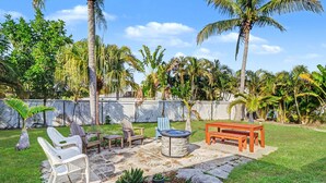 A backyard with a fire pit, outdoor furniture, and a variety of tropical plants.