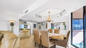 A spacious dining area with a large table and chairs, a chandelier, and a view through a glass door. - Beachfront condo with multiple balconies heated pool gym hot tub and AC (Clearwater Beach)