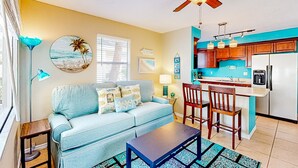A living room with a sofa, coffee table, and a dining area with chairs and a kitchen counter.