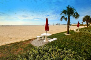 A beachside area with white tables and red umbrellas, palm trees, and a clear sky. - Seaside bliss with scenic Gulf view balcony and beachfront heated pool and spa (Indian Shores)