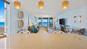 Amplia sala de estar con una isla de cocina grande, muebles de mimbre y un balcón con vista al océano.