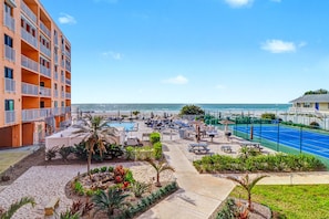 A beachfront hotel with a pool, tennis court, and multiple balconies.