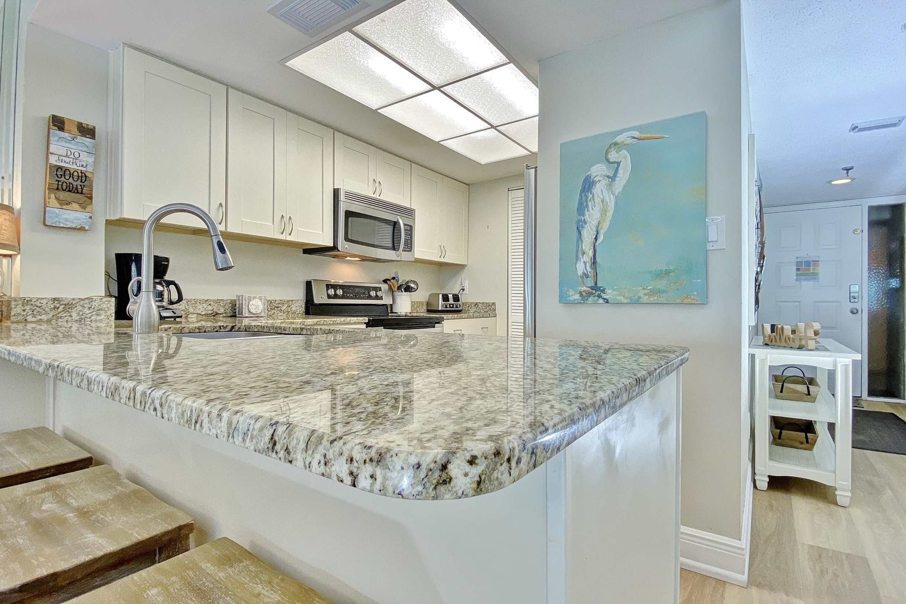 A kitchen with white cabinets, a granite countertop, a stainless steel sink, and a microwave.