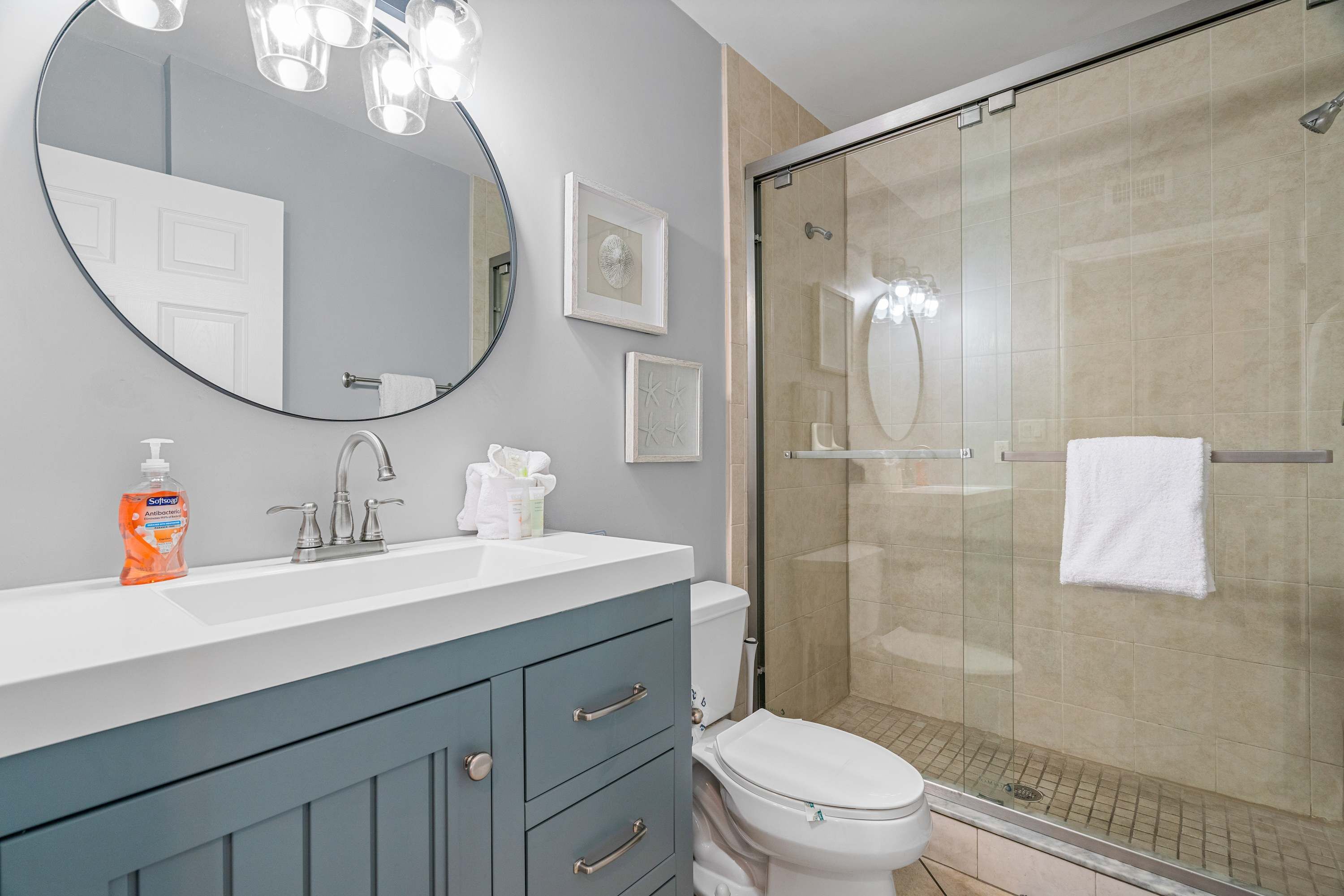 A bathroom with a white sink, a mirror, a glass shower enclosure, and a toilet.