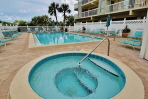 A swimming pool with lounge chairs and a small hot tub.