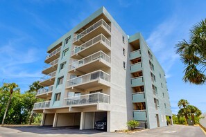 A multi-story residential building with balconies, parking spaces, and a clear sky.