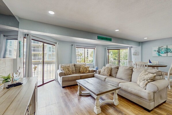 A spacious living room with a large beige sectional sofa, a wooden coffee table, and a dining area with a small table and chairs.