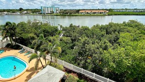 A hotel with a swimming pool, surrounded by lush greenery and a lake view.