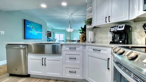 A modern kitchen with white cabinets, stainless steel appliances, and a large island. - 4th floor beachfront condo with private balcony views pool BBQ and AC (Indian Shores)