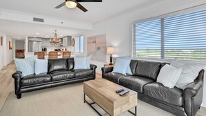 Ein geräumiges Wohnzimmer mit zwei schwarzen Ledersofas, einem Holztisch und einem Deckenventilator.