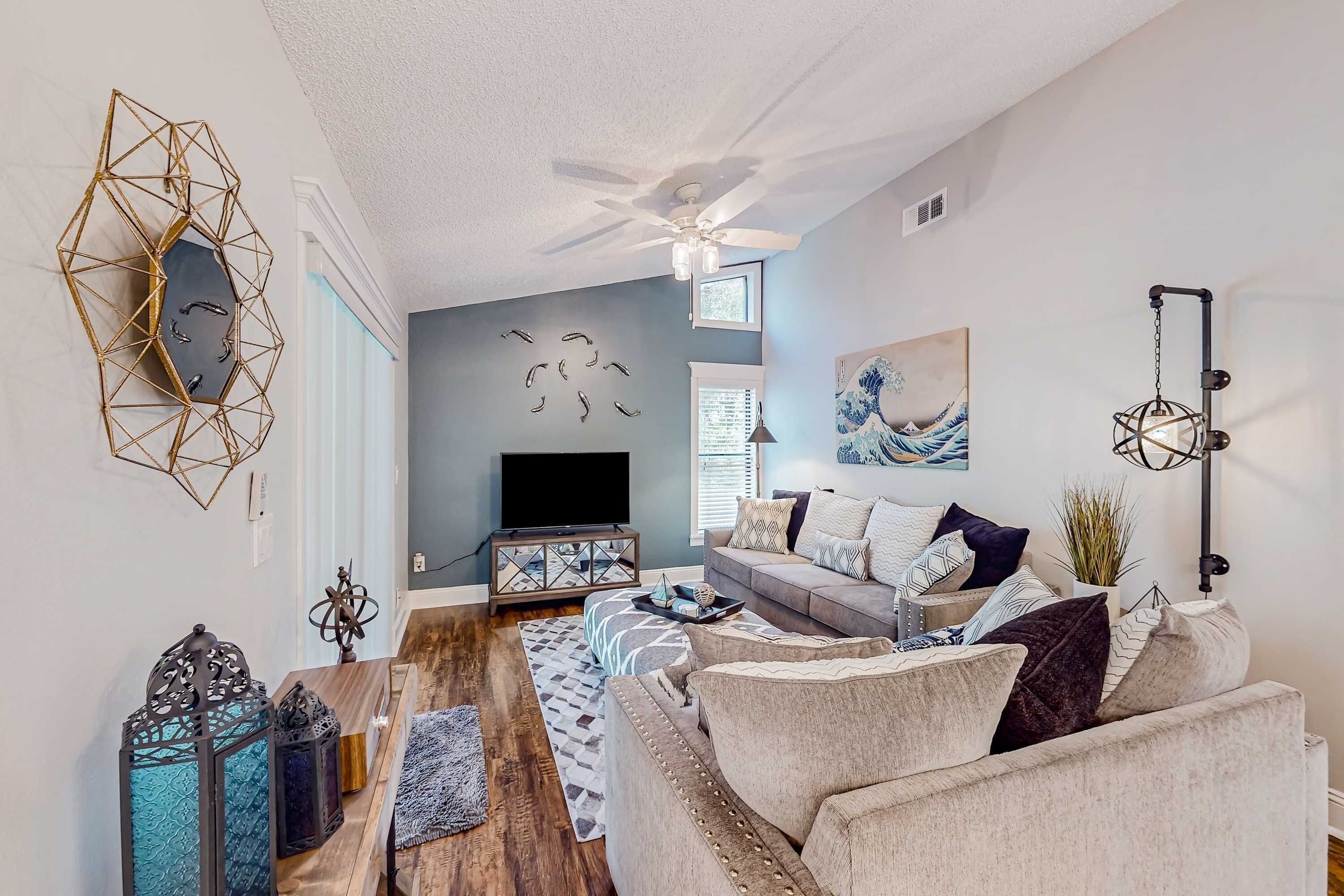 A modern living room with a ceiling fan, a TV, a sofa, and decorative wall art.
